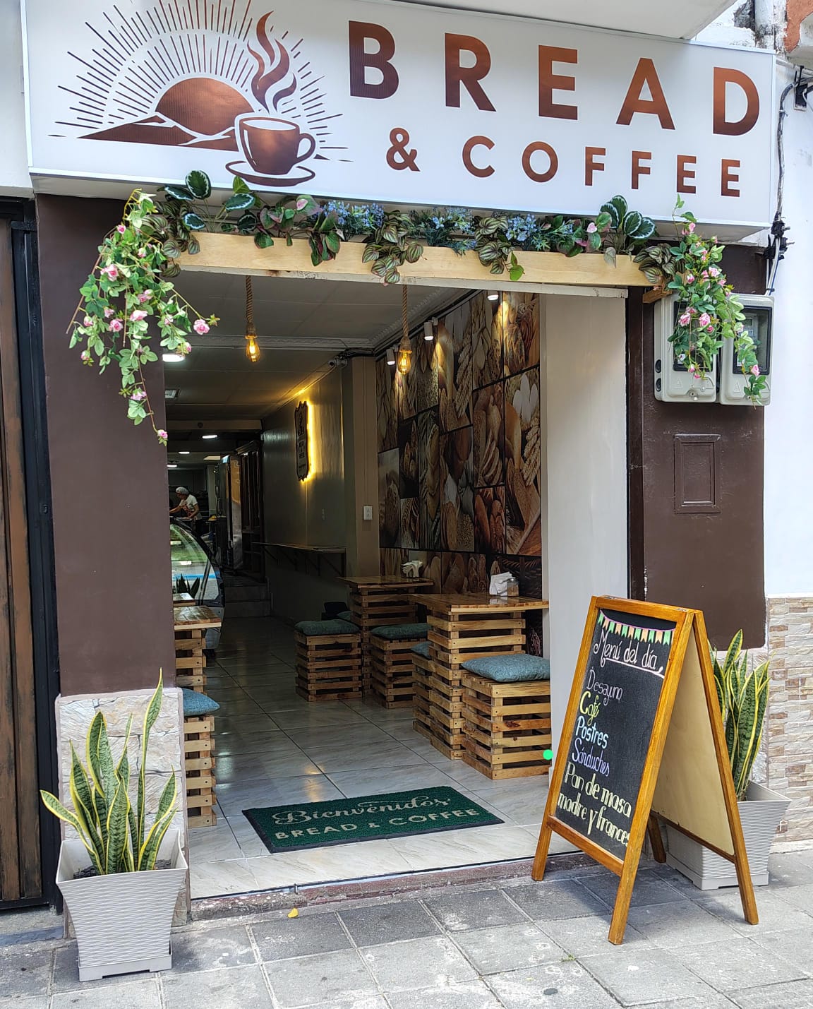 Fachada de Bread & Coffee con su letrero, flores y mesas de madera